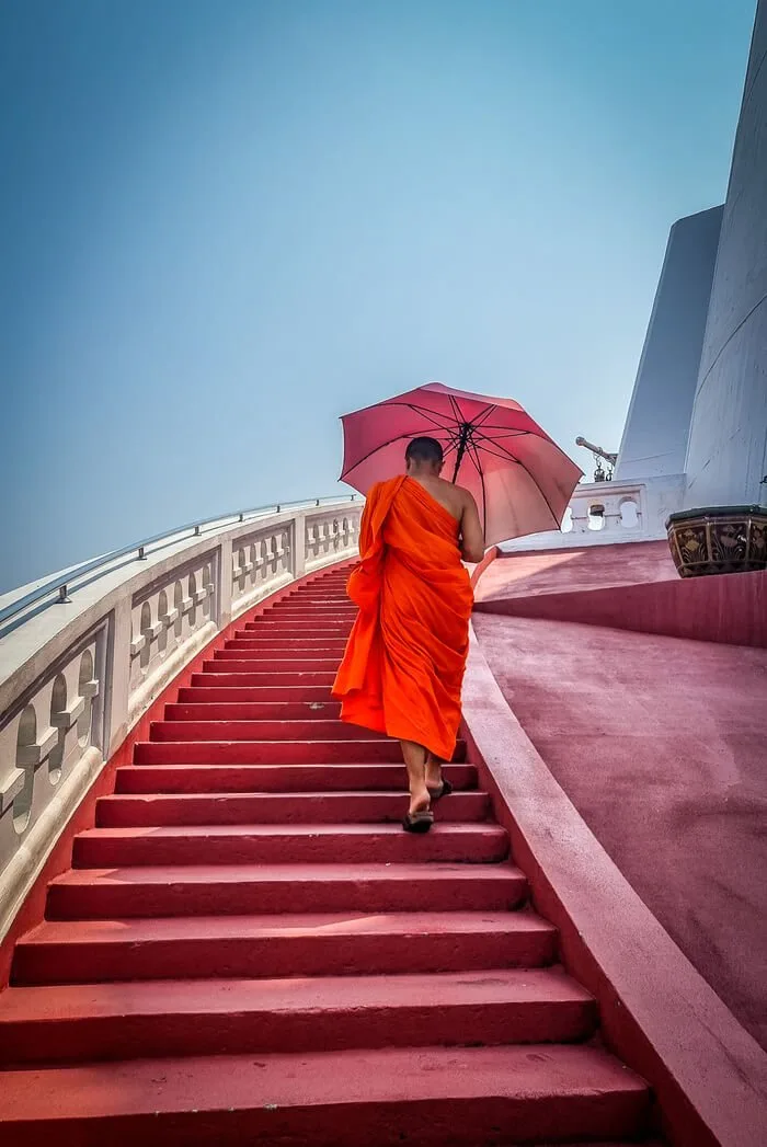 monk walking up steps of temple in bangkok